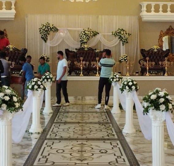 Aisle of white Roman pillars topped with white flowers and draped fabric