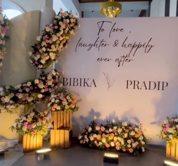 Script welcome wall with the couple's names, framed by flowers and warm lights