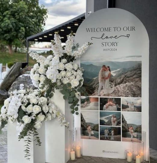 Arched 'Welcome to our love story' board with a photo collage and white flowers