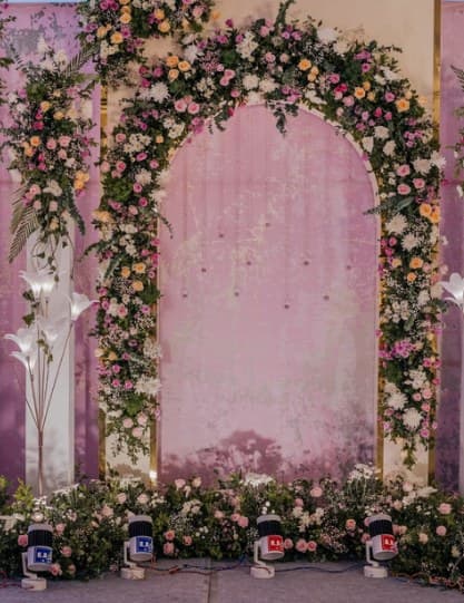 Pink arched backdrop wrapped in a garden-flower arch with uplights