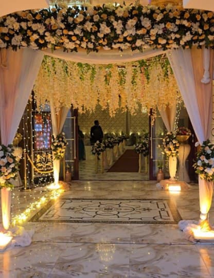 Hall entrance with a white floral canopy, hanging wisteria, drapes and lit flower pillars
