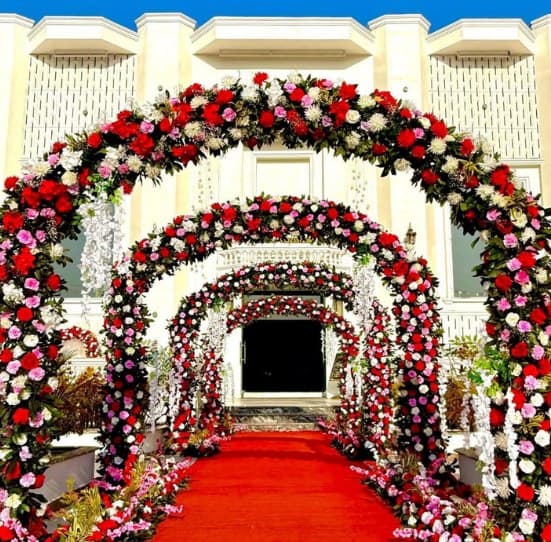 Tunnel of red, pink and white rose arches over a red carpet leading to the venue