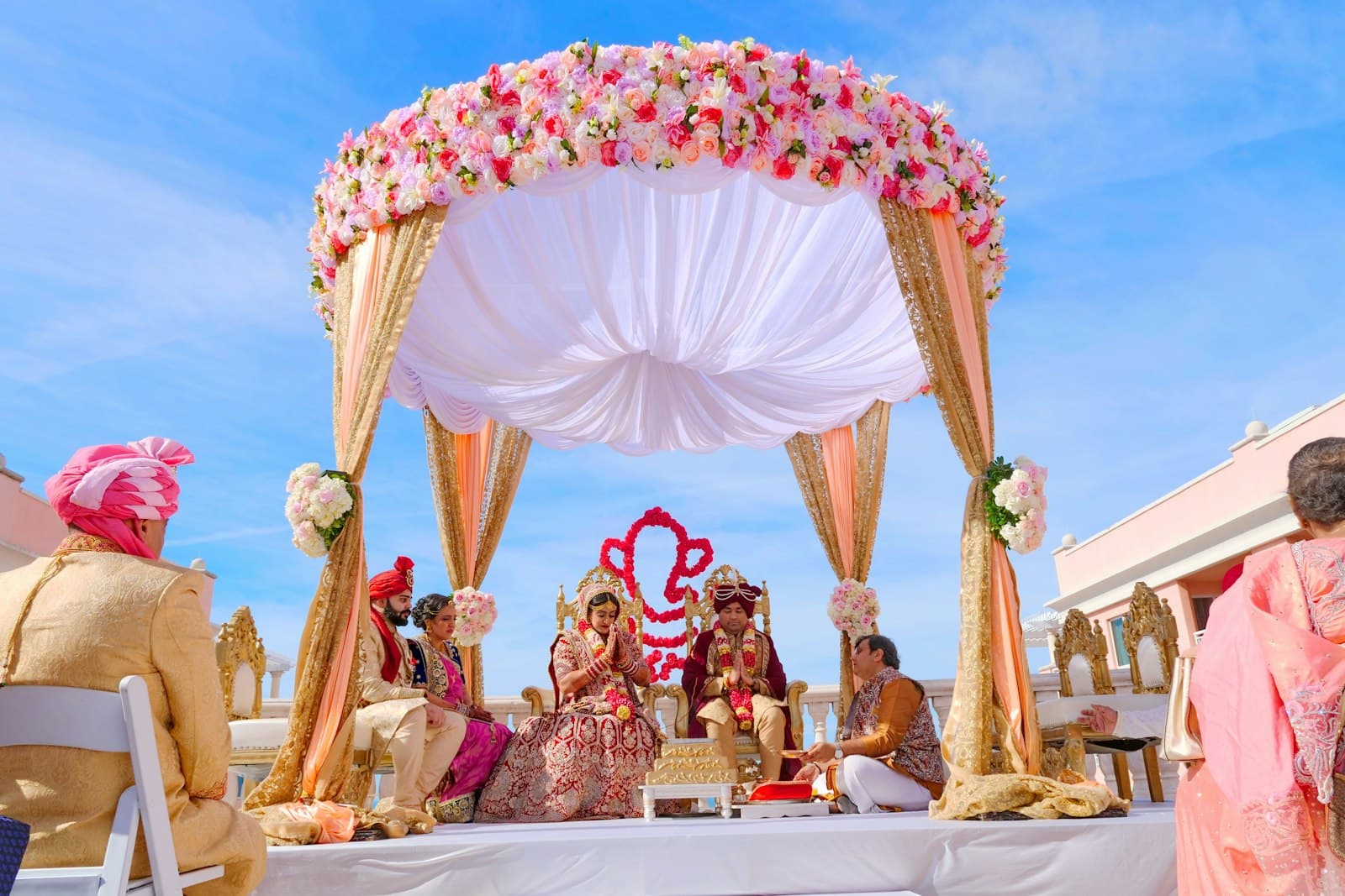 Outdoor wedding ceremony under a rose-covered mandap with draped ivory fabric