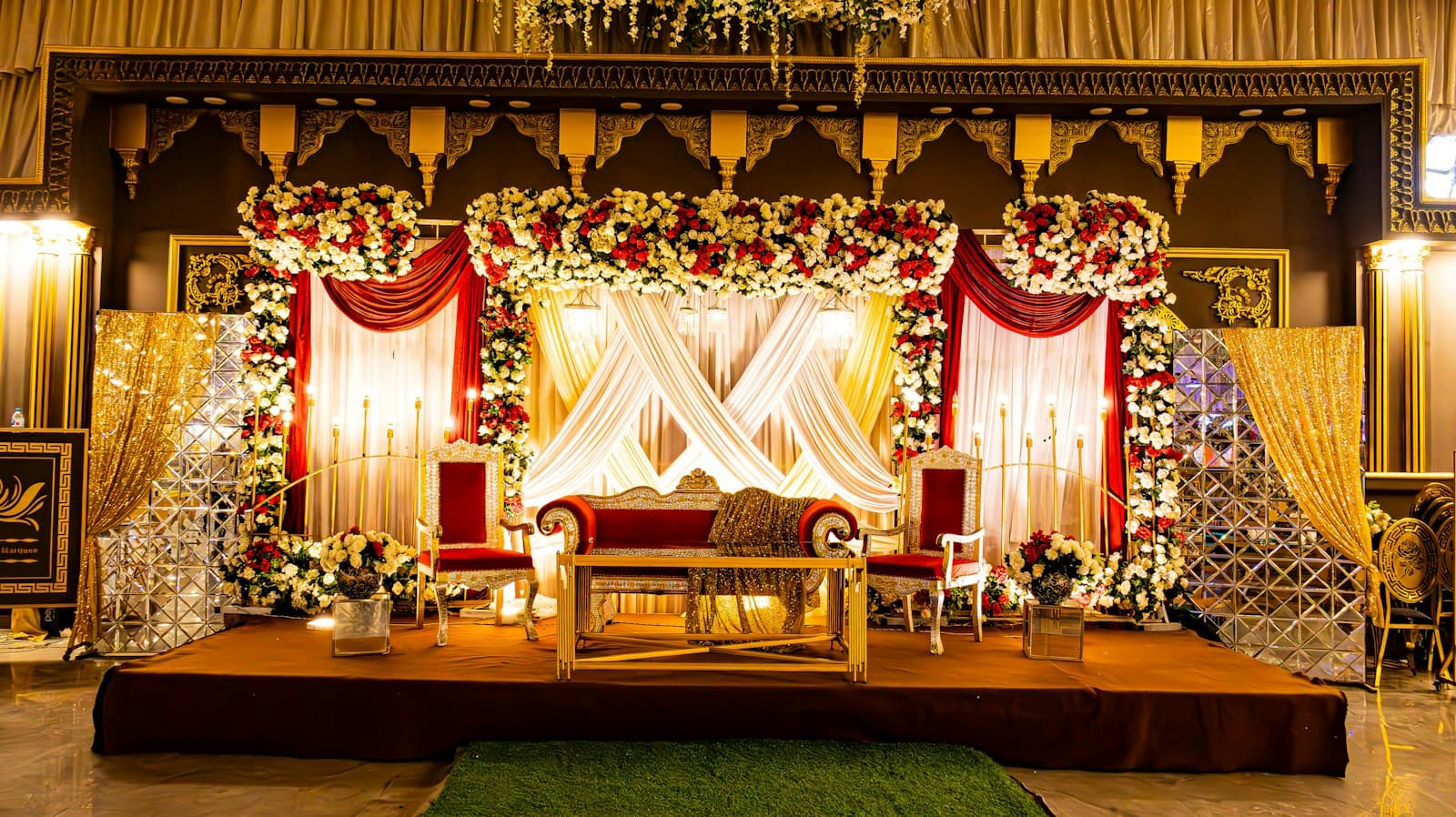 Reception stage framed in red and white roses with a crossed ivory drape and a velvet sofa