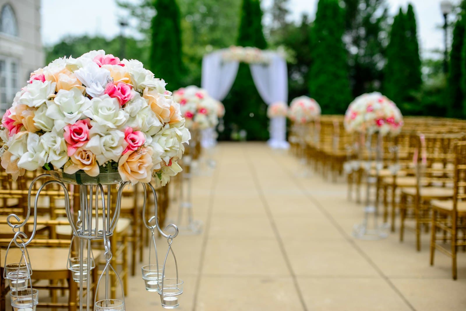 Aisle lined with rose arrangements on tall stands, leading to a draped floral arch